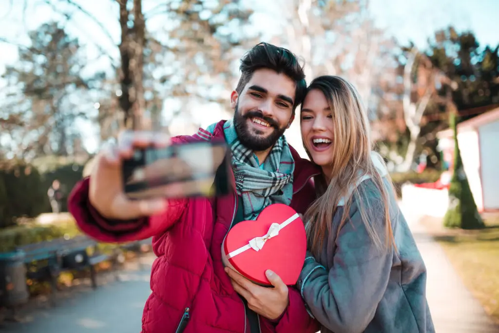 Casal sorridente tirando selfie com caixa em formato de coração