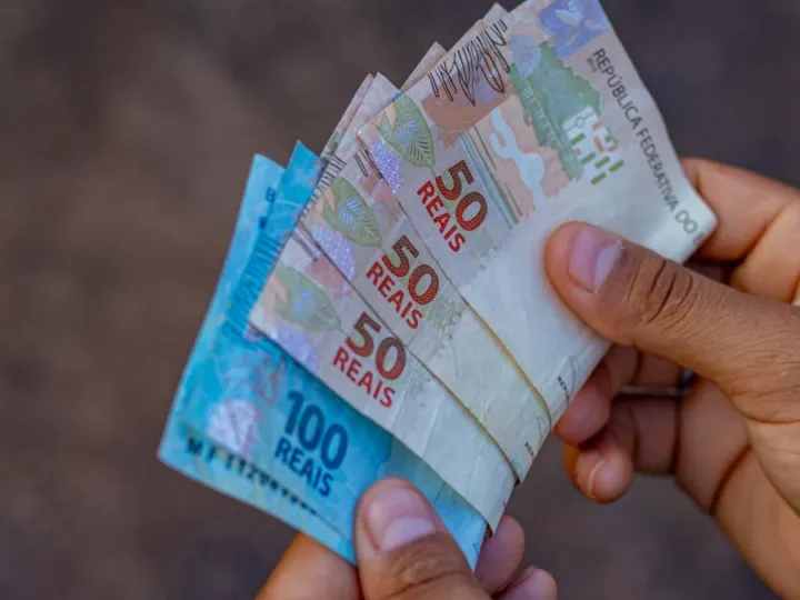 Foto de uma pessoa com notas de 100 e 50 reais na mão