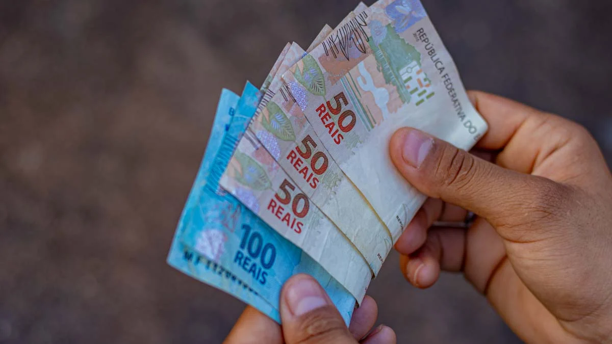 Foto de uma pessoa com notas de 100 e 50 reais na mão