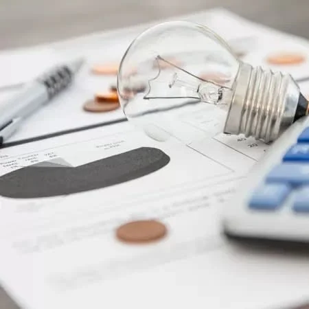 Lâmpada, calculadora e moedas sobre conta de energia elétrica desfocada
