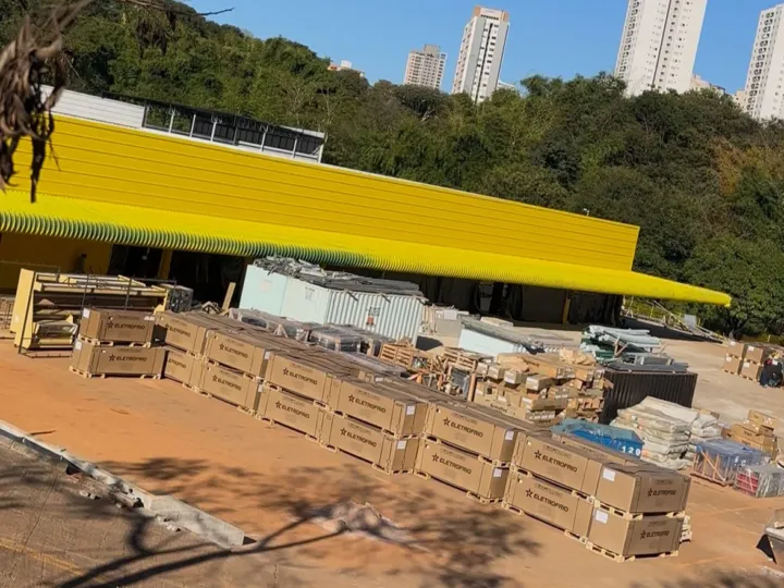 Imagem aérea de uma unidade de atacarejo em Anápolis, Goiás, com fachada ampla em cores vivas. E alguns materiais de construção ao redor
