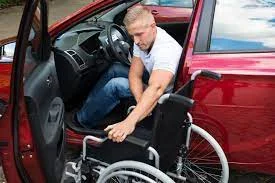 Homem com deficiência física se preparando para sair de um carro adaptado, posicionando a cadeira de rodas ao lado do veículo