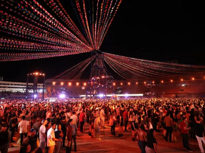 Multidão em um animado arraial noturno, com bandeirolas coloridas e iluminação típica de festa junina.