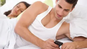 Homem usa o celular enquanto a mulher enquanto esconde o celular atrás dela, olhando para a tela de forma desconfiada.