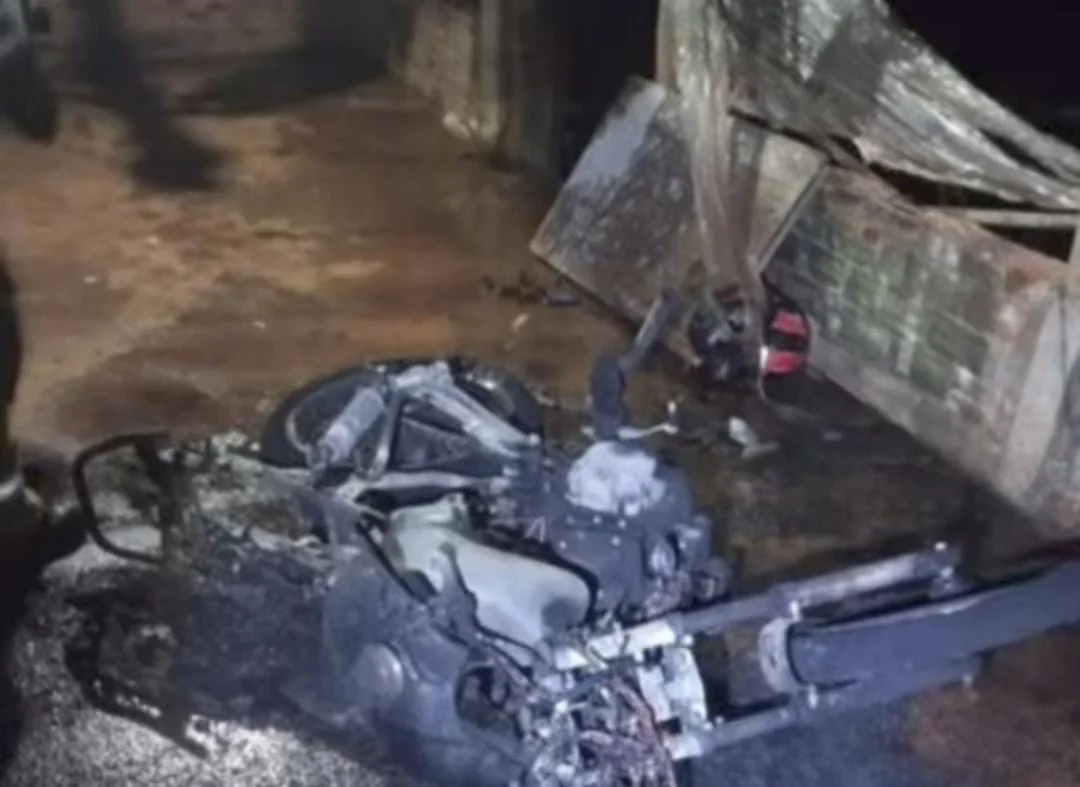 Motocicleta carbonizada ao lado de um portão queimado após incêndio em via pública de Anápolis.