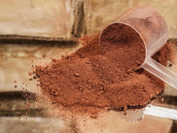 Suplemento em pó de cor achocolatada derramado com colher medidora transparente