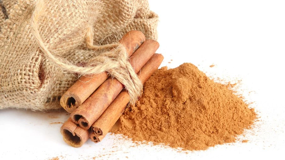 Canela em pau amarrada ao lado de canela em pó sobre fundo branco