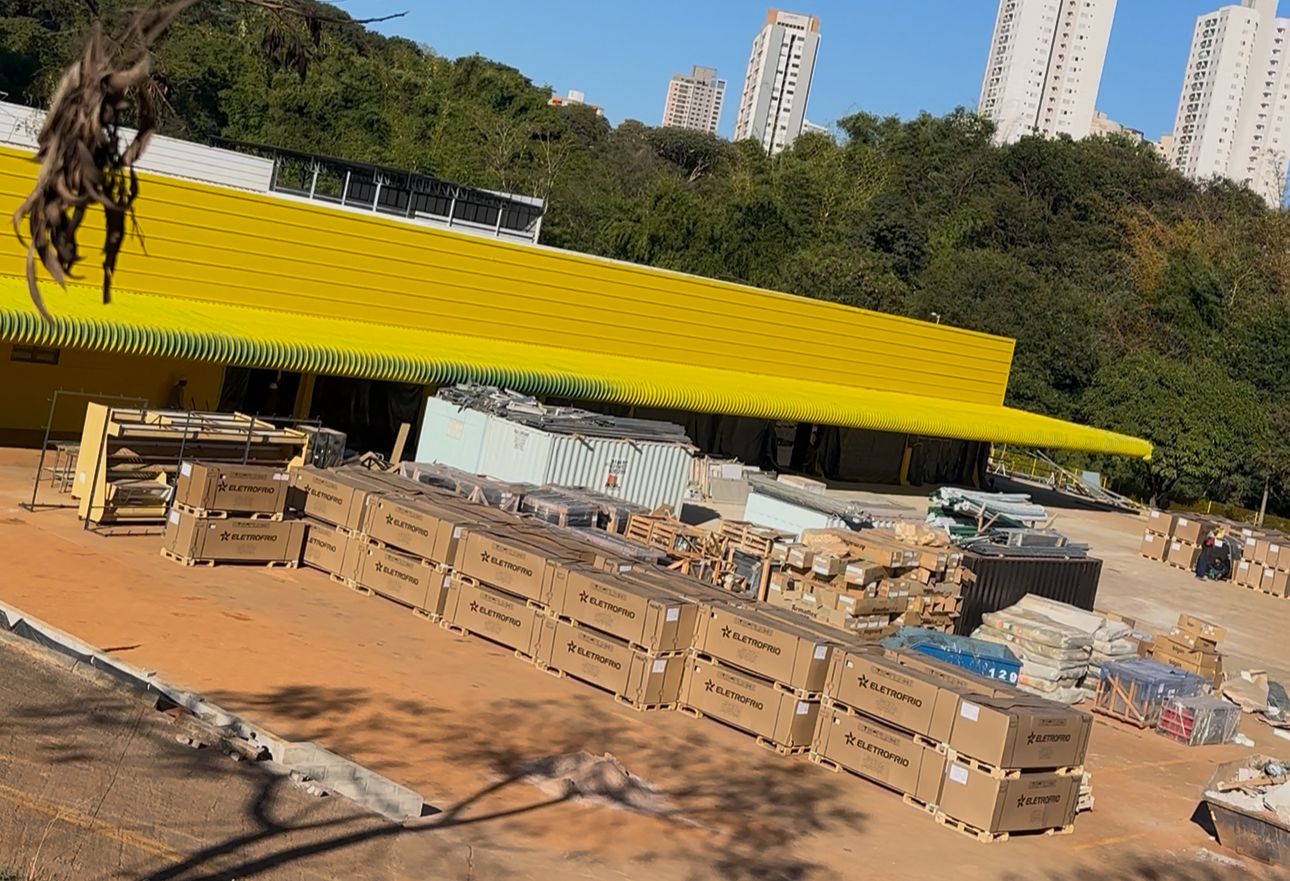 Imagem aérea de uma unidade de atacarejo em Anápolis, Goiás, com fachada ampla em cores vivas. E alguns materiais de construção ao redor