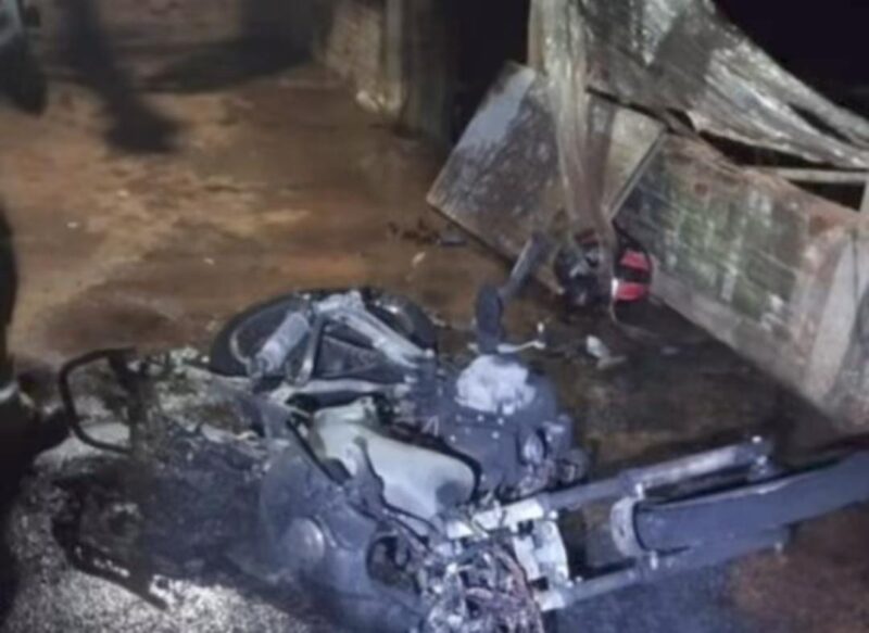 Motocicleta carbonizada ao lado de um portão queimado após incêndio em via pública de Anápolis.