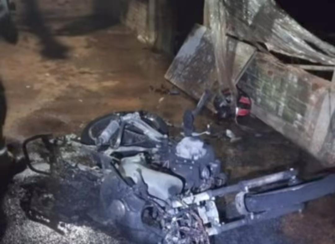 Motocicleta carbonizada ao lado de um portão queimado após incêndio em via pública de Anápolis.