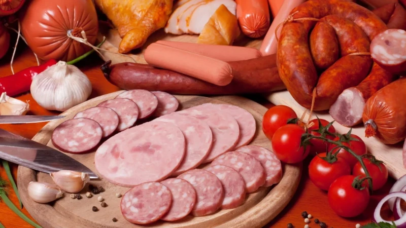 Variedade de carnes processadas como salame, presunto, salsichas e linguiças em tábua de madeira