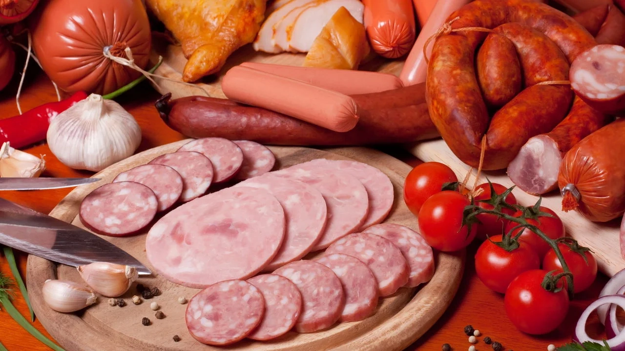 Variedade de carnes processadas como salame, presunto, salsichas e linguiças em tábua de madeira