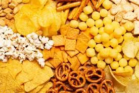 Mesa com salgadinhos industrializados, biscoitos, batata frita, pipoca e snacks variados