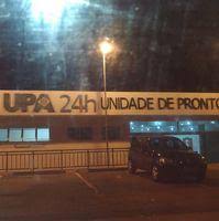 Imagem noturna da fachada de uma Unidade de Pronto Atendimento (UPA) 24 horas. O prédio aparece com a iluminação acesa e um carro estacionado na frente. O letreiro "UPA 24h Unidade de Pronto Atendimento" está visível na parte superior do edifício.