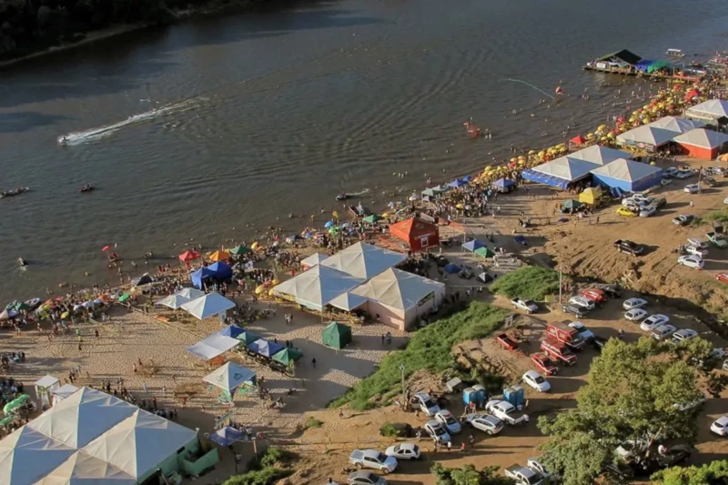 Imagem aérea mostra praia cheia de turistas e barracas no Vale do Araguaia.