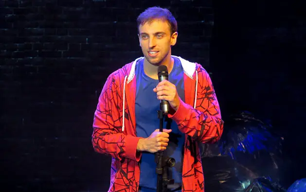 Léo Lins durante apresentação de stand-up com blusa vermelha e microfone em mãos no palco