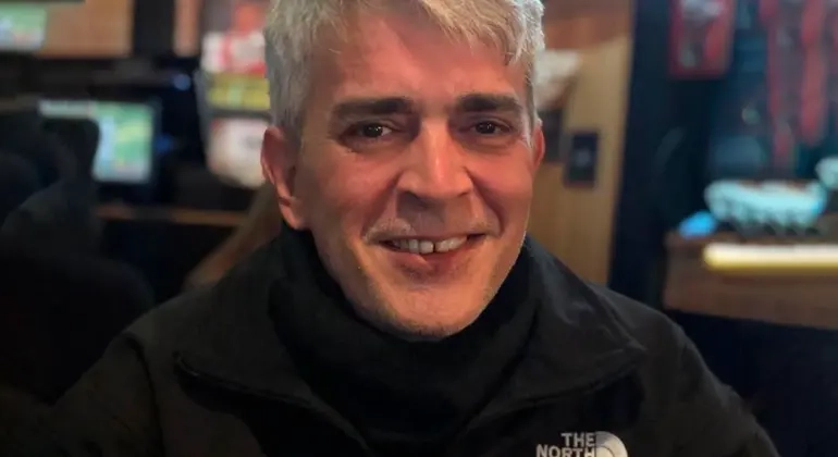 Marco Antônio de Oliveira Viu em ambiente fechado, sorrindo, usando blusa preta com logo da The North Face


