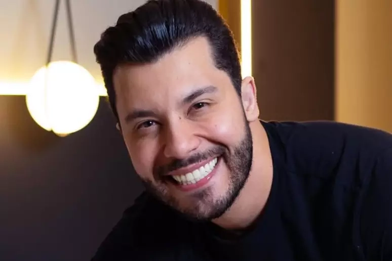 Murilo Huff sorrindo em local fechado com iluminação amarelada ao fundo