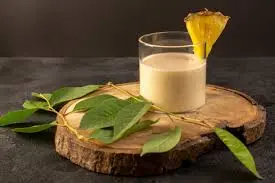 Copo de suco de inhame decorado com fatia de abacaxi sobre uma base de madeira, com folhas verdes ao lado.