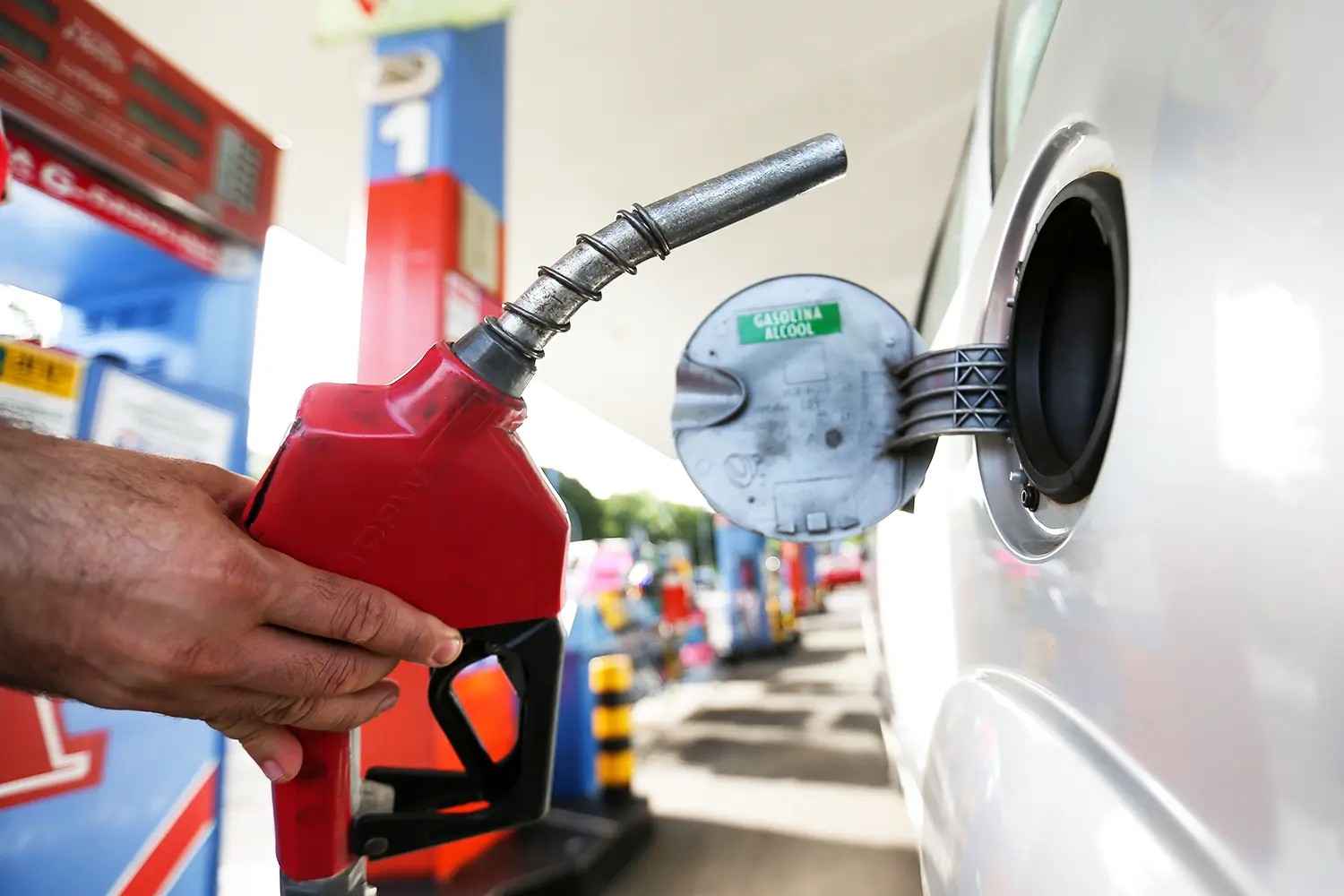 Bico de bomba de combustível sendo inserido no tanque de um carro em um posto de gasolina.