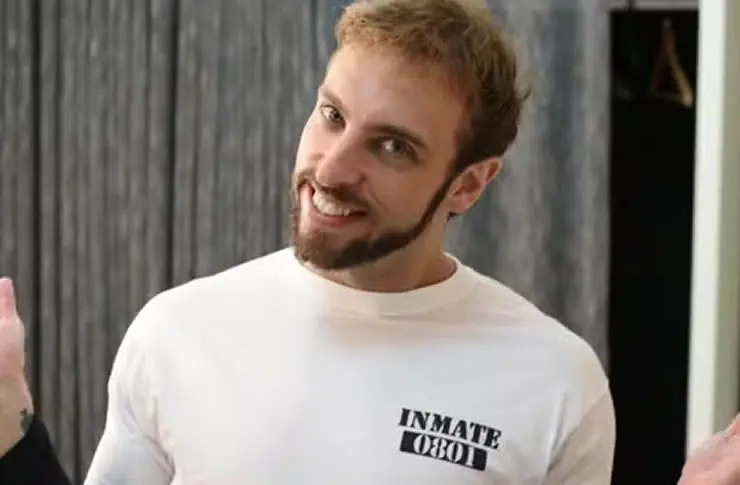 Leo Lins sorrindo com uma camisa branca e um fundo cinza
