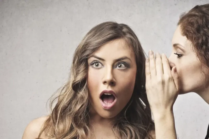 Mulher com expressão de choque enquanto ouve segredo de outra mulher