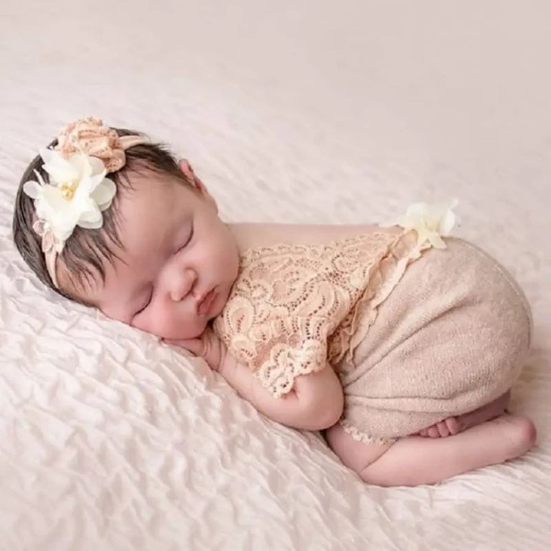 Bebê recém-nascida dormindo de lado com roupa rendada e faixa floral na cabeça.