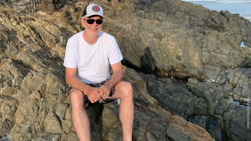 Professor Marco Antônio sentado em rochas, sorrindo, usando camiseta branca e boné
