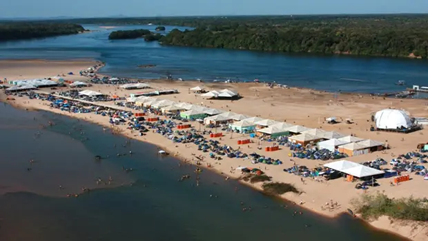 Praia lotada de barracas e estruturas à beira do Rio Araguaia, durante temporada de veraneio.