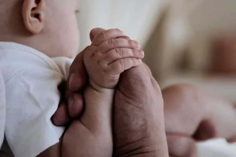Close das mãos de um bebê segurando o dedo de um adulto, simbolizando proteção e cuidado.