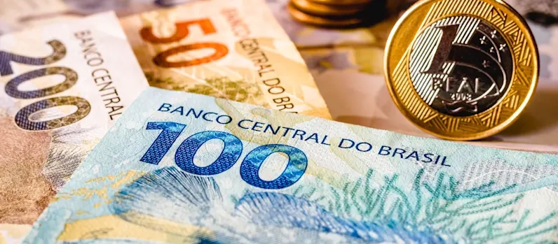 Notas de R$ 100, R$ 200 e moedas de R$ 1 real em cima de uma superfície.