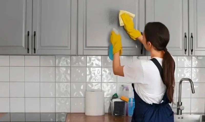 Mulher com luvas de borracha limpa armário de cozinha com pano e spray de limpeza.