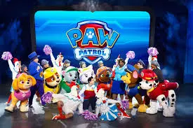 Personagens da Patrulha Canina em trajes coloridos no palco durante apresentação para crianças.