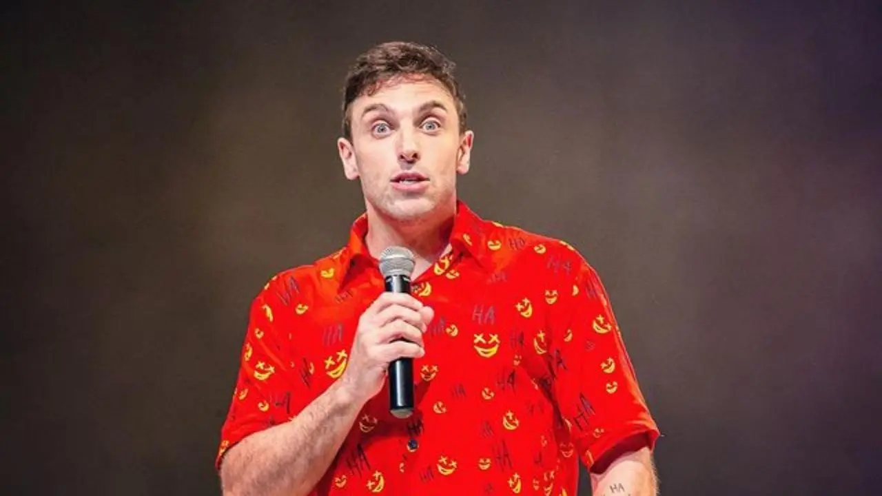 Léo Lins no palco com camisa estampada vermelha durante show “Enterrado Vivo”