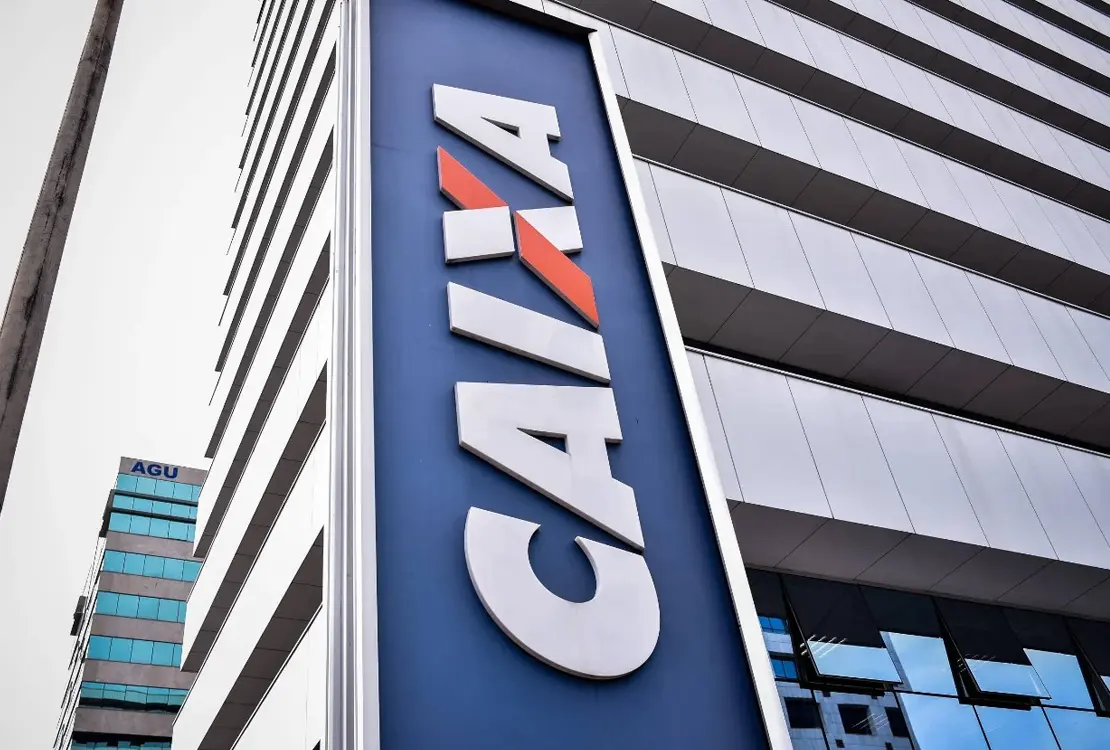 Fachada da Caixa Econômica Federal com logotipo em destaque e prédio espelhado ao fundo