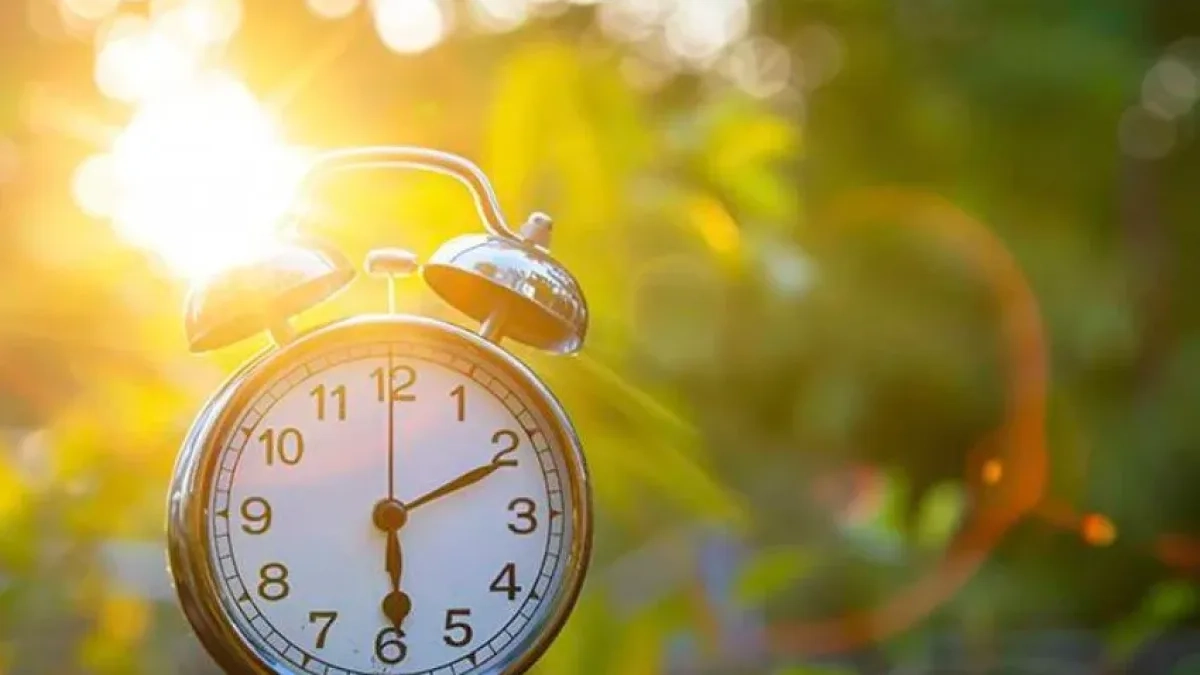 Mão segurando um pequeno relógio com o pôr do sol ao fundo, formando uma silhueta.