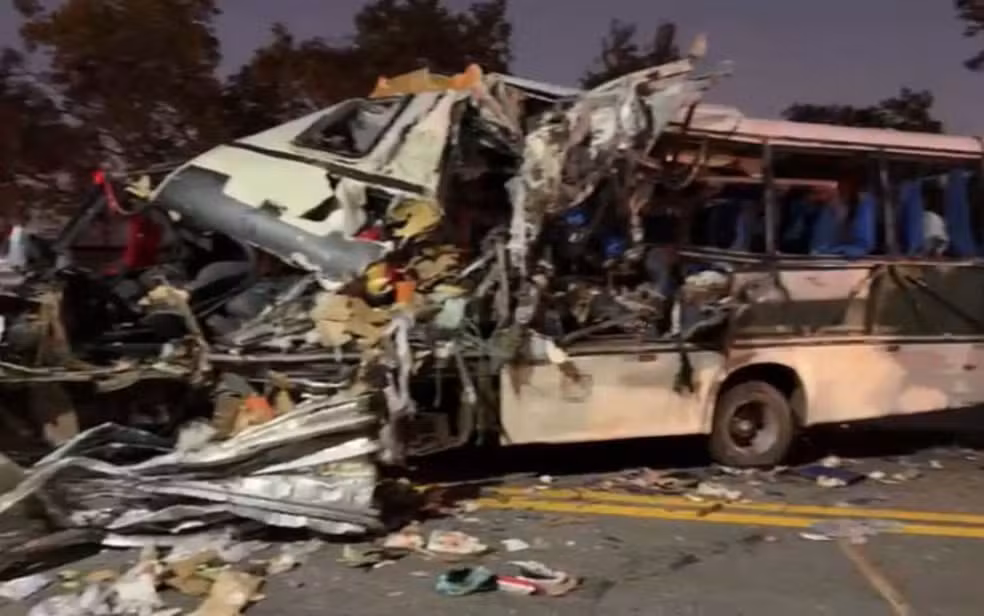 Frente de ônibus completamente destruída após colisão com carreta na BR-153; bombeiro e equipes de resgate trabalham no local do acidente.