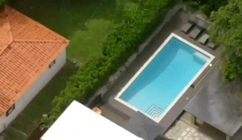 Imagem aérea de uma residência com telhado vermelho e uma piscina retangular cercada por área verde.