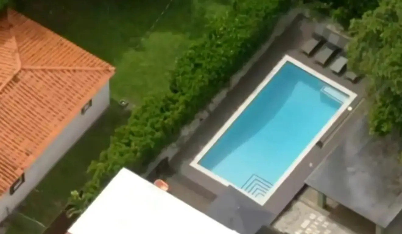 Imagem aérea de uma residência com telhado vermelho e uma piscina retangular cercada por área verde.