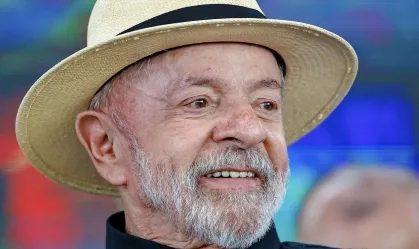 Presidente Lula sorrindo, usando um chapéu de palha claro, com fundo desfocado.