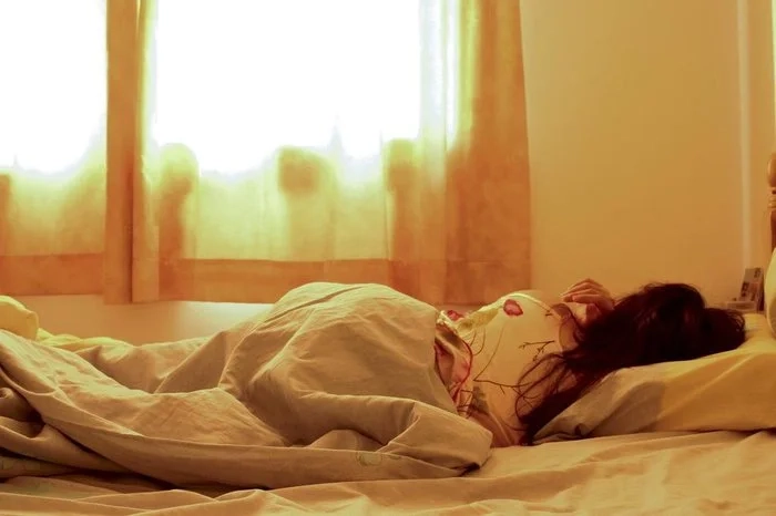 Mulher dormindo durante o dia em quarto iluminado por luz natural, simbolizando soneca da tarde