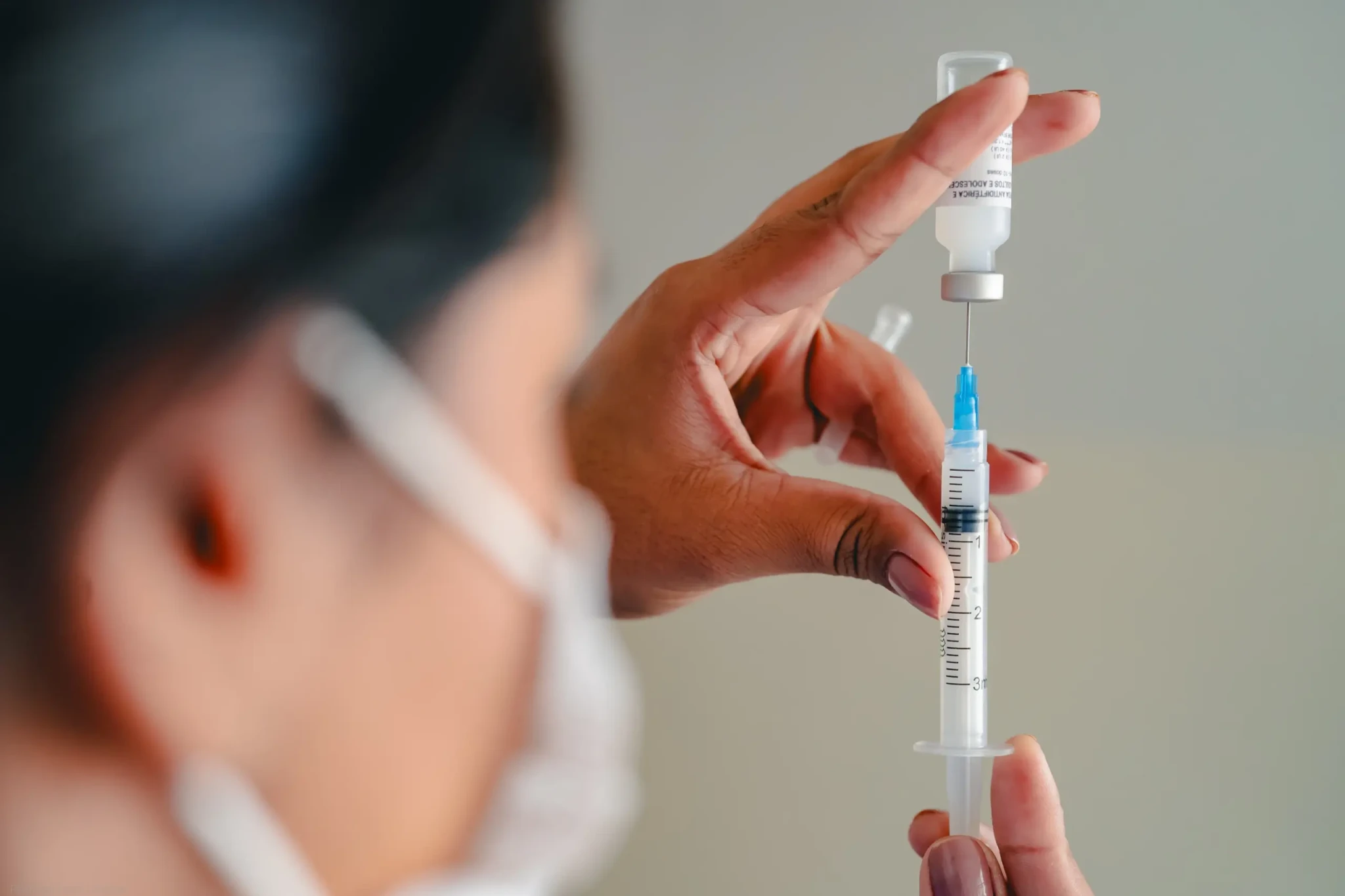 Enfermeira segura seringa e frasco de vacina em ambiente hospitalar com luzes desfocadas ao fundo