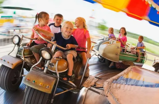 Crianças se divertem em brinquedo giratório no parque de diversões sob uma lona colorida
