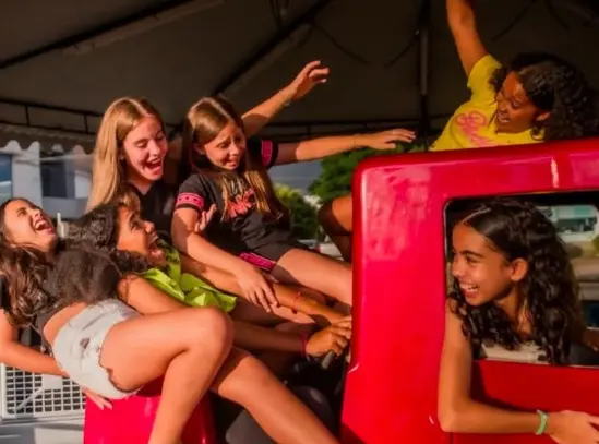 Grupo de meninas sorrindo e se divertindo em brinquedo vermelho no parque de diversões