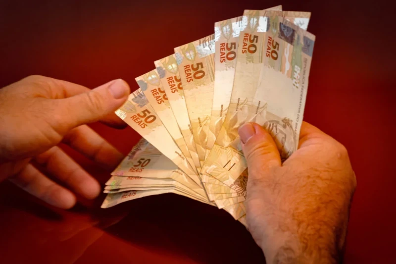 Imagem-colorida-mão-com-dinheiro-pagamento-moeda-papel-Metrópoles1-e1732828157915