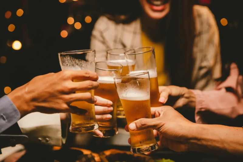 Pessoas brindando com copos de cerveja durante encontro em bar.