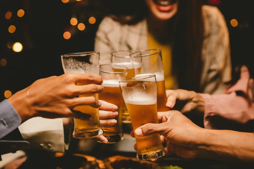 Pessoas brindando com copos de cerveja durante encontro em bar.