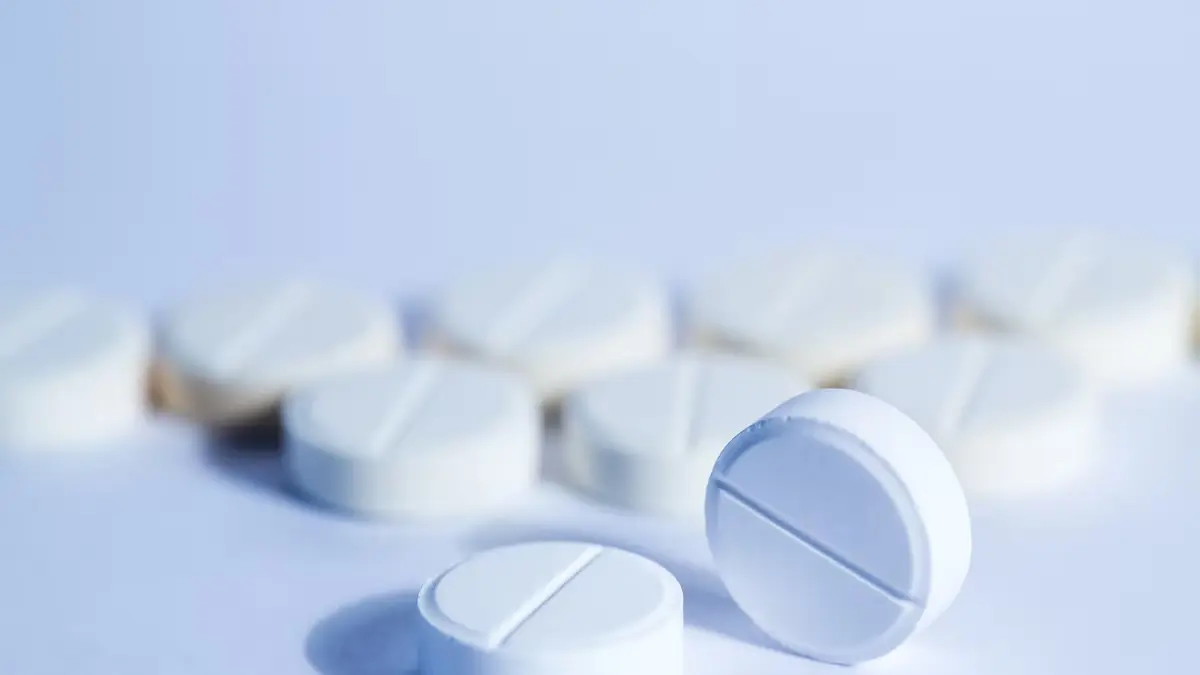 Comprimidos brancos sobre uma superfície clara, em imagem ilustrativa de medicamento.