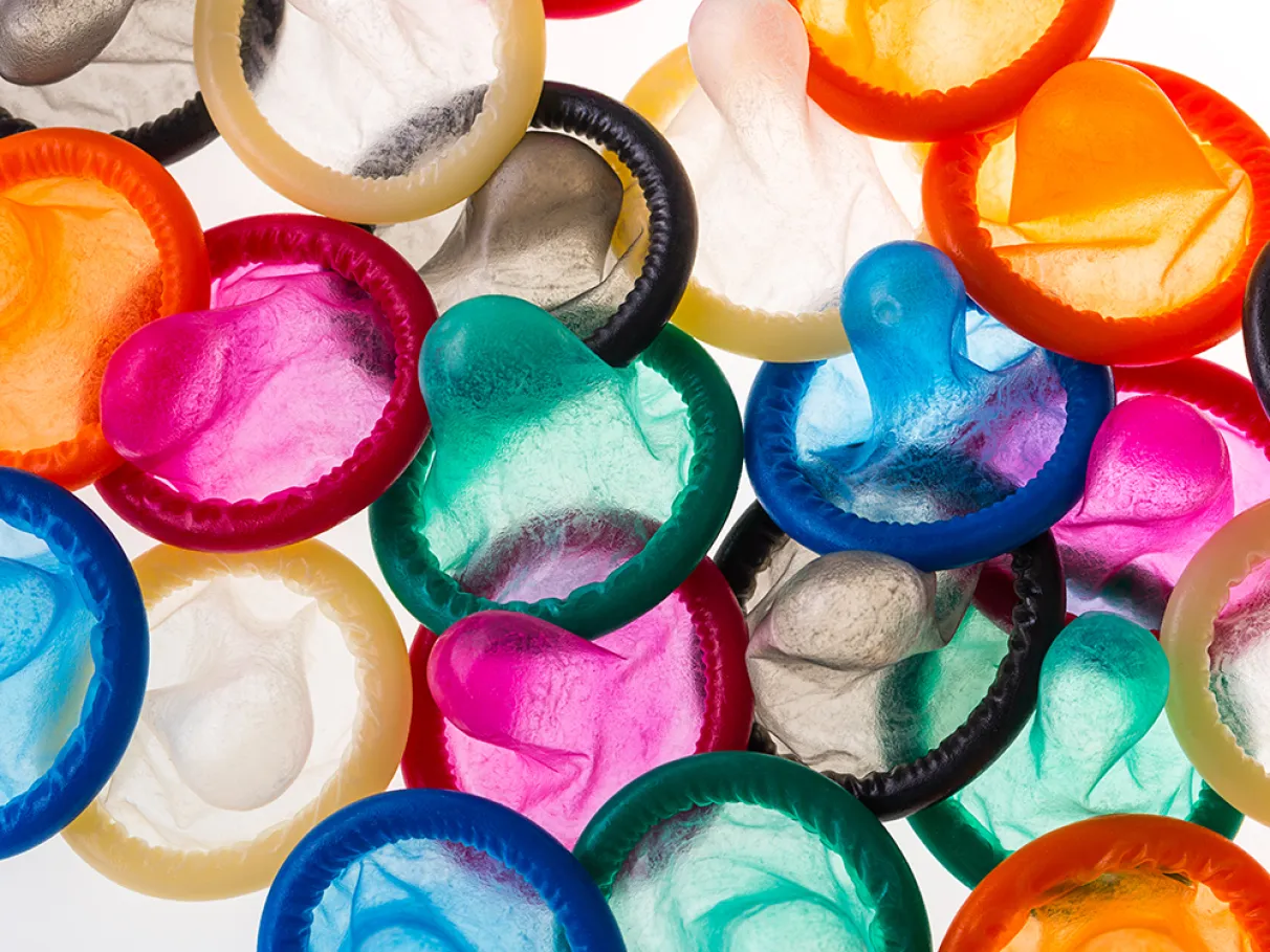 Preservativos coloridos espalhados sobre um fundo branco, representando prevenção contra infecções sexualmente transmissíveis.