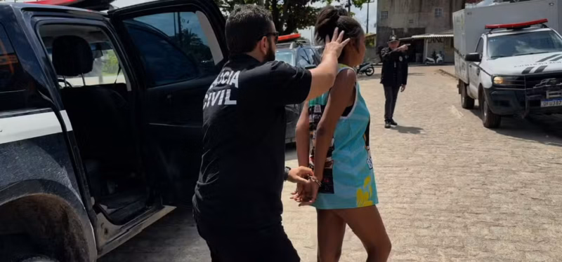 Mulher é conduzida por policial civil após ser presa por suspeita de matar o marido em Caaporã, na Paraíba.